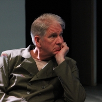 A man with grey hair leaning on his hand looking off to the side.