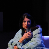 A woman cuddling in a blanket on a couch holding a glass of water